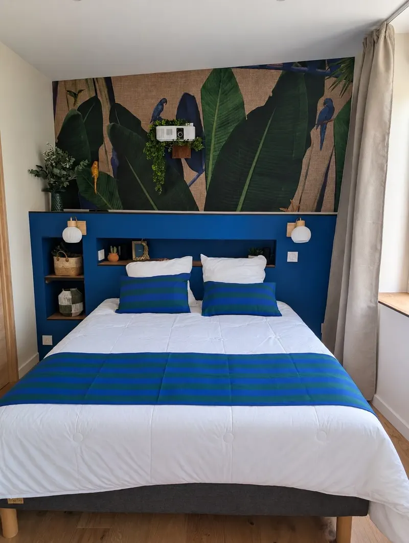 Chambre d'hôtes préparée : lit fait au cordeau, coussins bleus et papier peint tropical