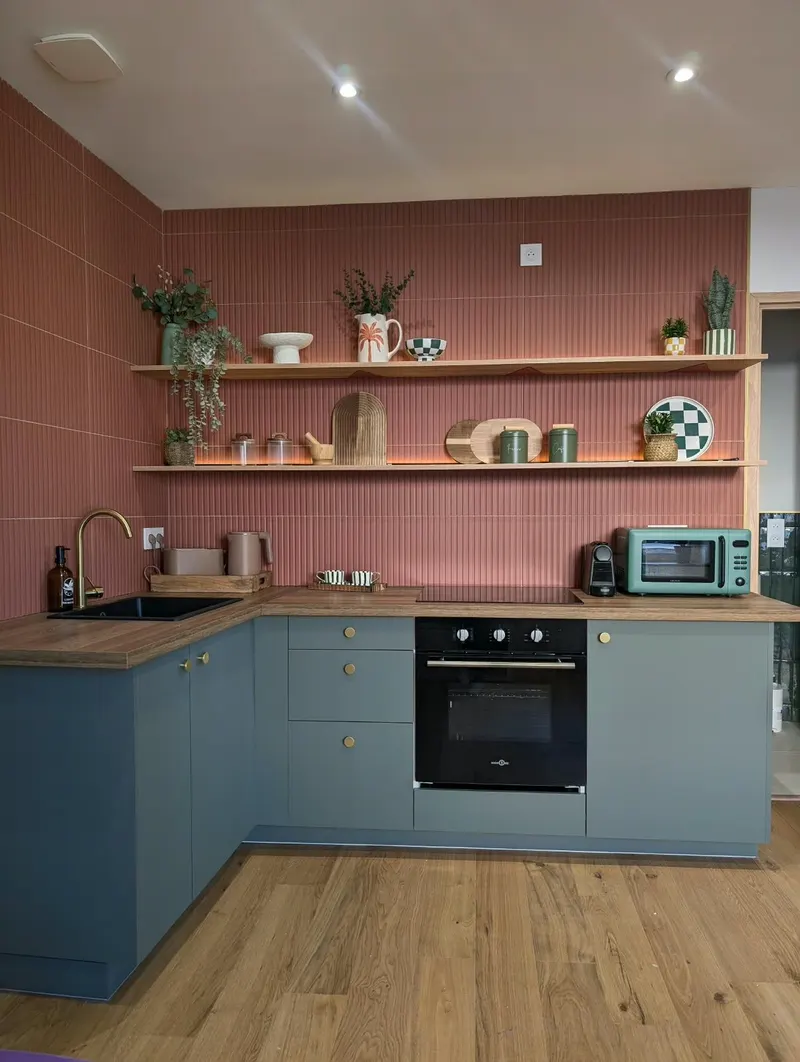 Cuisine équipée et rangée : étagères en bois, murs terracotta et meubles bleu-vert