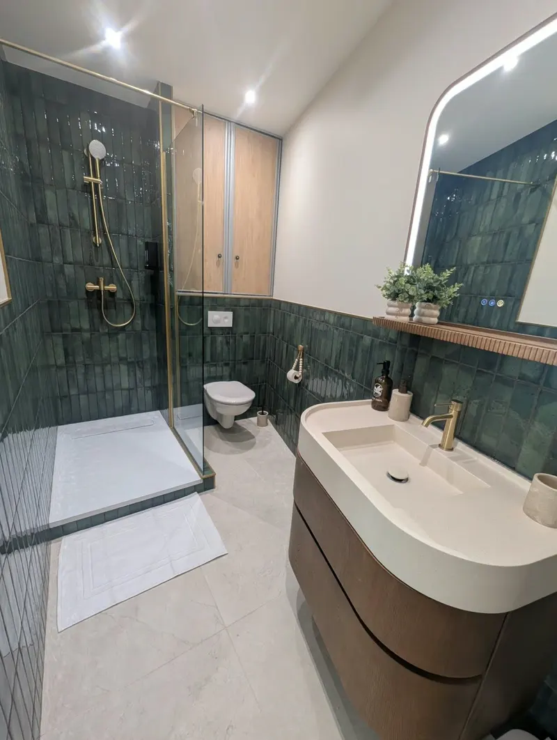 Salle de bain d'une location : vasque claire, carrelage vert et paroi de douche impeccable